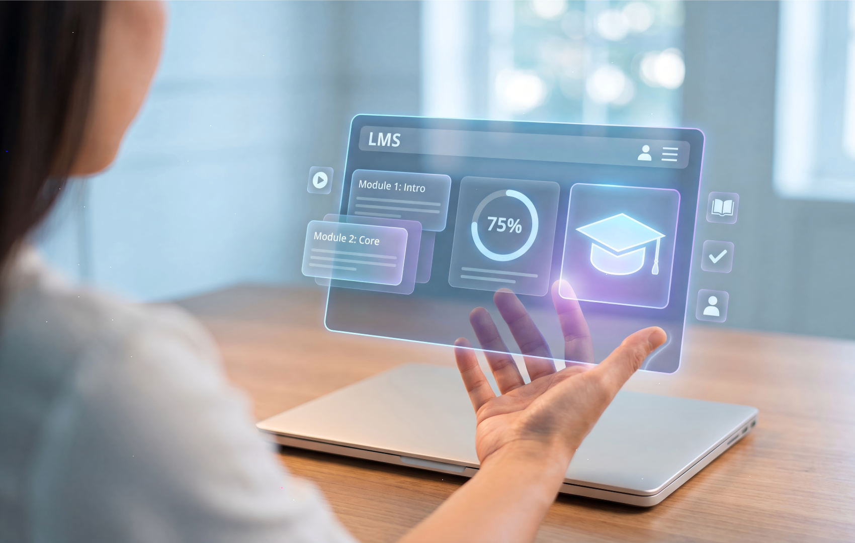 A person seated at a desk uses a transparent holographic tablet interface displaying an LMS dashboard with module cards and a graduation cap icon, with a laptop open beneath the floating screen.