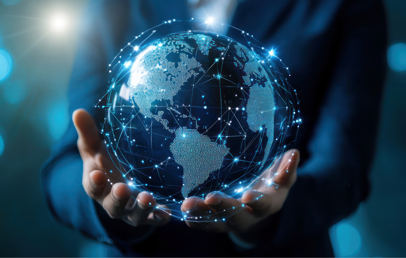 A person in a dark suit holds up a glowing digital globe with a network of blue lights and dots, set against a dark, softly blurred background with bright bokeh highlights.