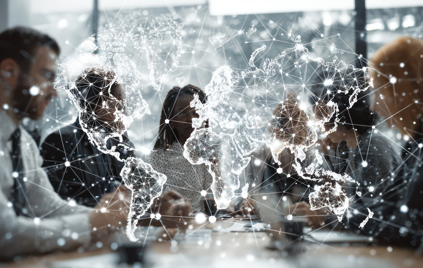 A group of business professionals collaborating around a table in a modern office, overlaid with a glowing white digital world map and network graphic.