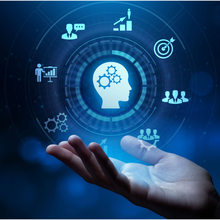 A glowing blue digital graphic showing a human hand supporting a floating holographic interface with a central white head silhouette, gears, business icons, and circular tech elements on a dark blue background.