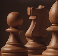 Close-up of wooden chess pieces, including pawns and a knight, in warm brown tones against a dark background.